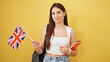 © Krakenimages.com - Young beautiful hispanic woman student smiling confident holding books and united kingdom flag over isolated yellow background