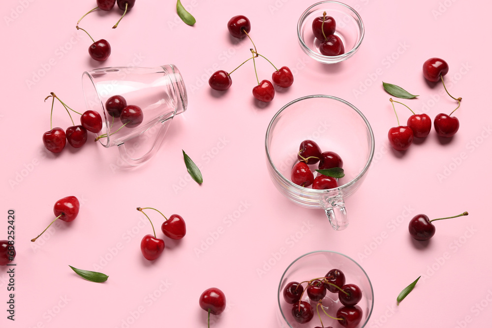 Glass cups and bowls with sweet cherries on pink background
