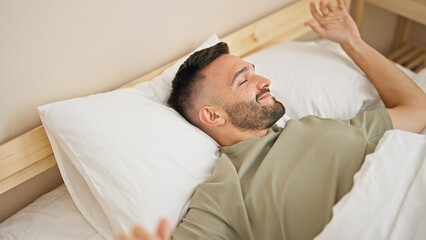 Canvas Print - Young hispanic man waking up stretching arms at bedroom