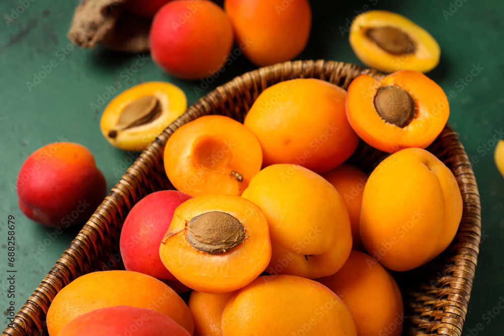 Wicker bowl with sweet apricots on green background
