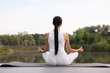 © New Africa - Woman practicing Padmasana on yoga mat outdoors, back view. Lotus pose