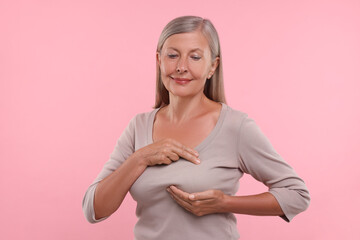 Poster - Beautiful senior woman doing breast self-examination on pink background