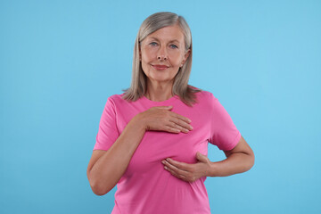 Wall Mural - Beautiful senior woman doing breast self-examination on light blue background