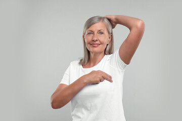 Poster - Beautiful senior woman doing breast self-examination on light grey background