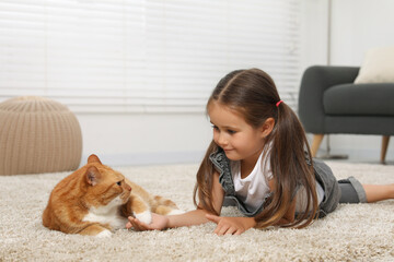 Poster - Smiling little girl and cute ginger cat on carpet at home