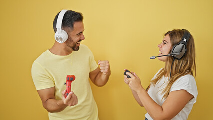 Poster - Man and woman couple playing video game celebrating over isolated yellow background