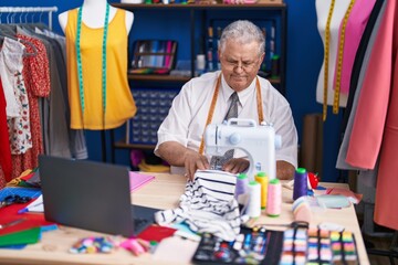 Poster - Middle age grey-haired man tailor using sewing machine and laptop at tailor shop