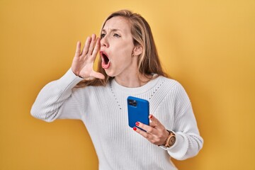 Sticker - Young blonde woman using smartphone typing message shouting and screaming loud to side with hand on mouth. communication concept.