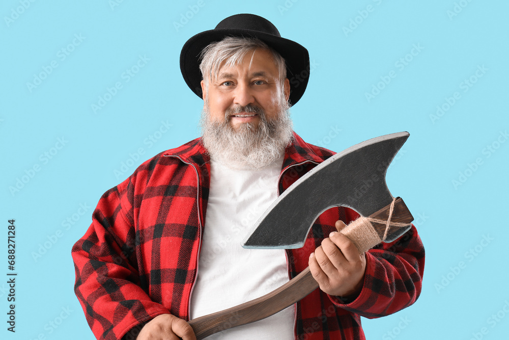 Portrait of mature lumberjack with axe on blue background