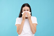 Suffering from allergy. Young woman blowing her nose in tissue on light blue background