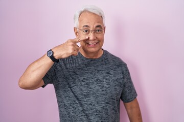 Canvas Print - Middle age man with grey hair standing over pink background pointing with hand finger to face and nose, smiling cheerful. beauty concept