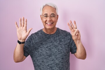 Wall Mural - Middle age man with grey hair standing over pink background showing and pointing up with fingers number eight while smiling confident and happy.