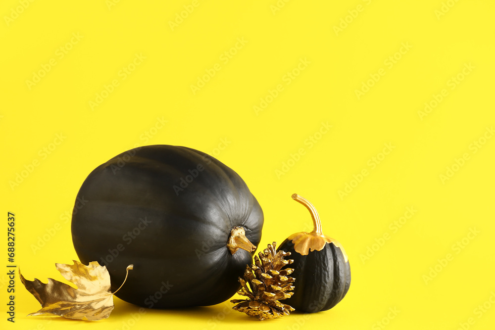 Black painted pumpkins with golden cone and leaf on yellow background