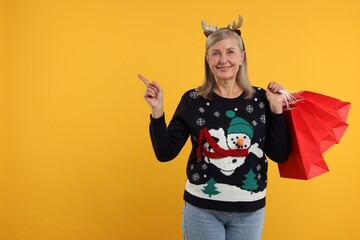 Sticker - Happy senior woman in Christmas sweater and deer headband with shopping bags on orange background. Space for text