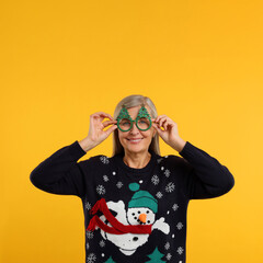 Sticker - Happy senior woman in Christmas sweater and funny glasses on orange background