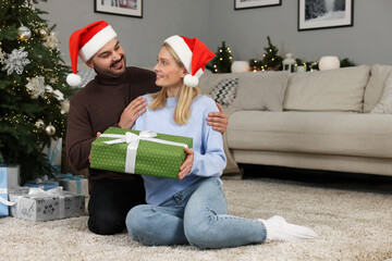 Wall Mural - Happy couple in Santa hats with Christmas gift at home