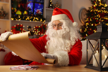 Canvas Print - Santa Claus reading letter at table in room decorated for Christmas