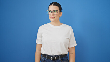 Poster - Young beautiful hispanic woman standing with serious expression looking to the side over isolated blue background