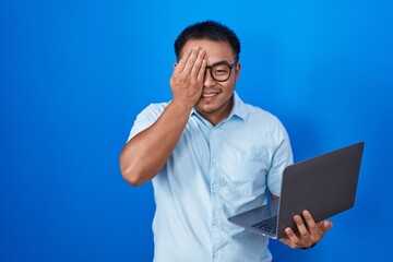 Sticker - Chinese young man using computer laptop covering one eye with hand, confident smile on face and surprise emotion.