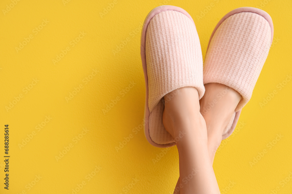 Female legs in soft slippers on yellow background