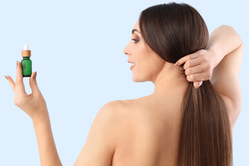 Wall Mural - Young brunette woman with hair serum on blue background, back view