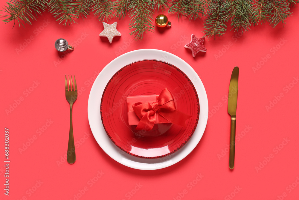 Beautiful table setting with fir branches, Christmas balls, candles and gift box on red background