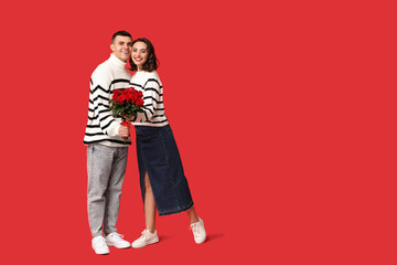 Poster - Loving young couple with bouquet of beautiful roses on red background. Celebration of Saint Valentine's Day