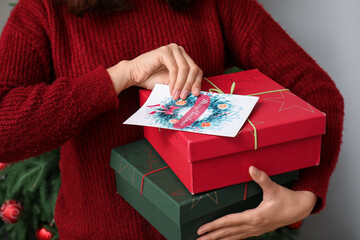 Canvas Print - Woman holding Christmas greeting card and gift boxes at home, closeup