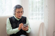 © N_studio - Asian senior man wearing headphone listening music with smartphone sitting on sofa for relax in living room at home, elderly wearing headset listening radio on smart phone, lifestyles concept.