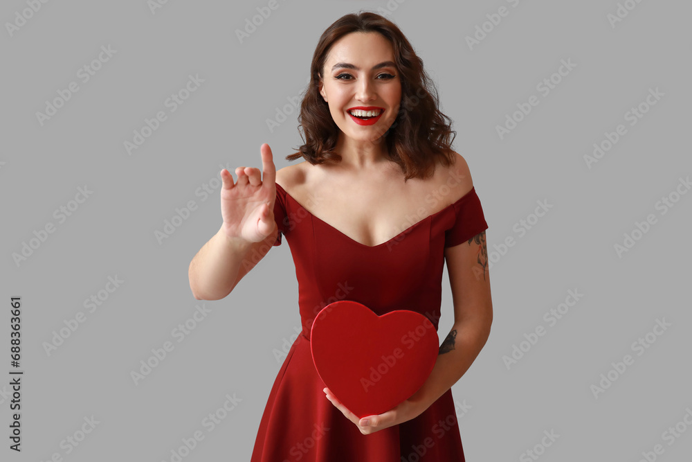 Happy young woman with gift box on grey background