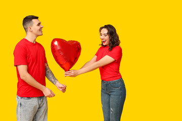 Poster - Loving young couple with heart-shaped balloon on yellow background. Celebration of Saint Valentine's Day