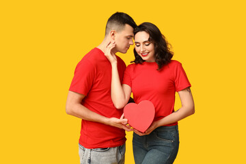 Poster - Loving young couple with gift box on yellow background. Celebration of Saint Valentine's Day