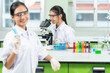 © Nutchapong Wuttisak - Two Asian female scientists are students. Looking through a microscope and holding a chemical test tube in a lab There is equipment for testing biology, glass tubes, pickers for medical work.
