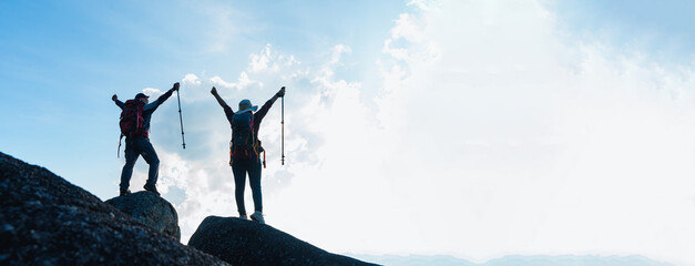 silhouette of asian male and female standing raised hands with trekking poles on cliff edge on top o