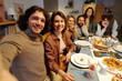 © pressmaster - Happy young couple taking selfie with members of their family while sitting by served festive table and enjoying Hanukkah dinner