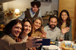© pressmaster - Happy young Jewish man with smartphone taking selfie of large family or communicating in video chat during Hanukkah dinner at home
