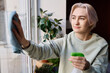 © AnnaStills - Young woman spraying and wiping window from dust during housework at home