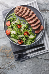 Wall Mural - Tagliata di manzo Italian style beef steak served with arugula, cherry tomatoes and parmesan close-up in a plate on the table. Vertical top view from above