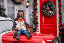 Little African American Boy With Sister Girl Sits On The Hood Christmas Vintage Car. Children Hugs