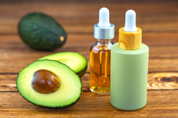 Wall Mural - Avocado and cosmetic bottles with oil on a wooden table. Concept of natural cosmetics and skin care.