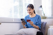 © David - Mobile Shopping. Cheerful Asian Woman Using Smartphone Shopping Online Holding Credit Card Making Payment Sitting At Sofa At Home. Internet Banking Application And E-Commerce