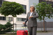 © New Africa - Being late. Worried senior businesswoman with red suitcase looking at watch outdoors