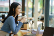 © Songsak C - Beautiful young asian business woman drinking coffee and using laptop computer while working in office.