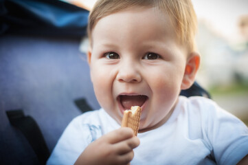 Wall Mural - Portrait of happy and smilling cute baby boy eating his favorite child biscuit. Healthy nutrition for kids concept