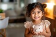 © Danko - Little indian girl with piggy bank and money at home