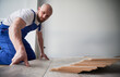 © anatoliy_gleb - Man in work overalls installing laminate floor in apartment under renovation. Male construction worker laying laminate timber flooring in living room with white wall on background.