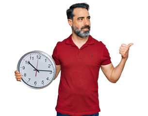 Sticker - Middle aged man with beard holding big clock pointing thumb up to the side smiling happy with open mouth