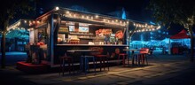 Food Truck Selling Burgers And Drinks. Empty Scene, With Table Chairs And Umbrellas, Nighttime Atmosphere