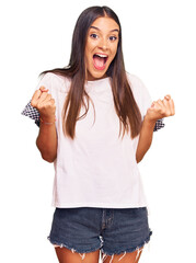 Wall Mural - Young hispanic woman wearing casual clothes celebrating surprised and amazed for success with arms raised and open eyes. winner concept.