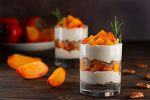 Dessert in a glasses with persimmon, rosemary, pecan, whipped cream and biscuit on a wooden table. Healthy food, vegan, sugar, gluten and lactose free.
